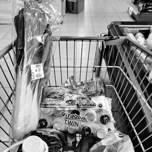 A shopping trolley holding groceries and leafy vegetables in a supermarket.